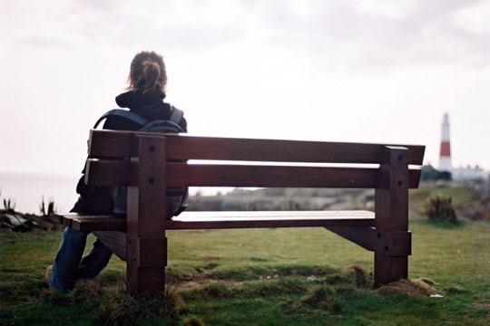 Das Foto zeigt ein Mädchen von hinten, das auf einer Bank sitzt.