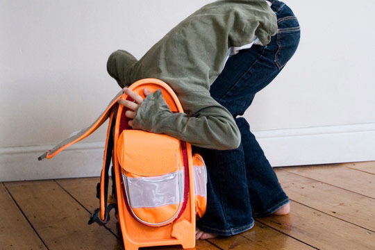 Das Foto zeigt ein Mädchen, das ihren Kopf im Schulrucksack, der vor ihr auf dem Boden steht, versteckt.