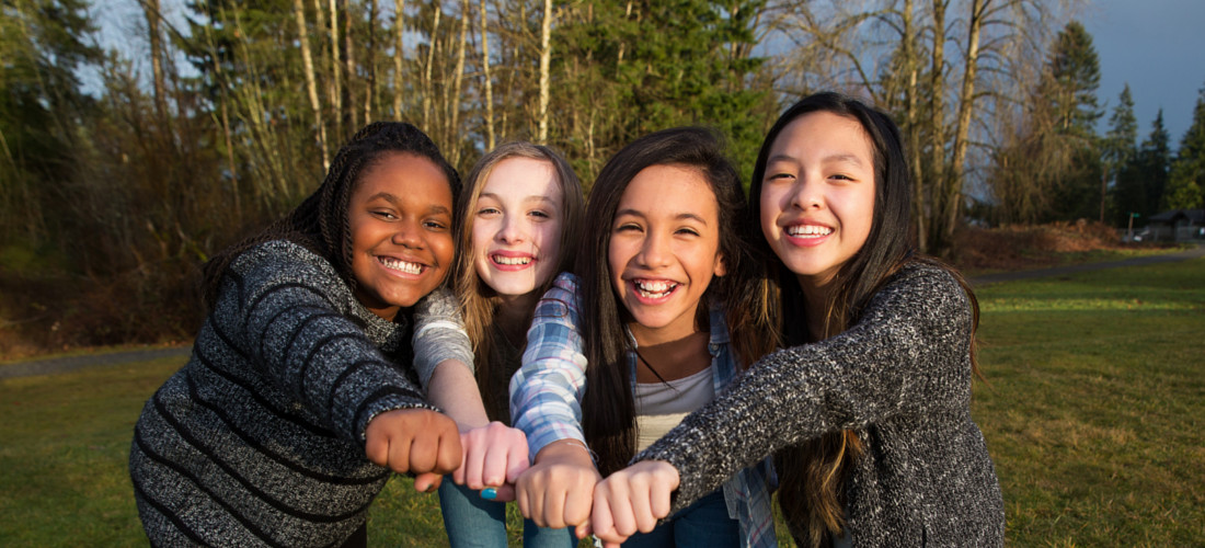 Das Foto zeigt vier Mädchen die ihre Fäusten zusammen stecken. Die Mädchen lachen und zeigen Zusammenhalt.